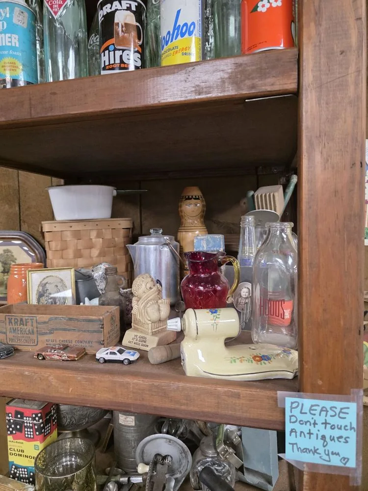 A shelf of antique bottles, tins and kitchenware inside the store, with a handwritten sign asking visitors not to touch
