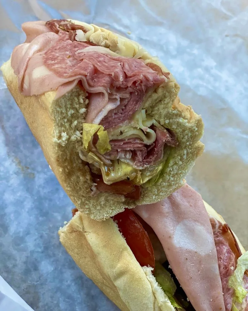 An Italian grinder cut in half, packed with cold cuts, lettuce and tomato