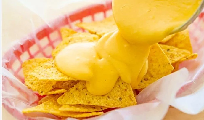 A basket of nachos with cheese sauce being poured over