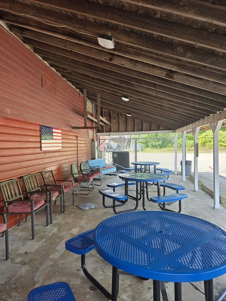 The covered side porch with blue tables and chairs under the red board siding